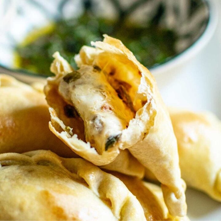 Shows a cheese empanada split in half resting on top of more golden empanadas.