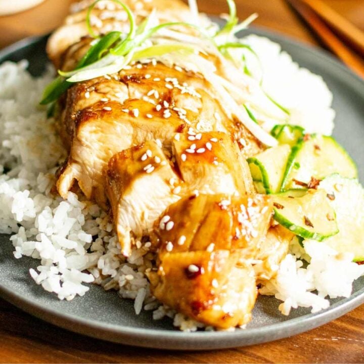 A plate of sliced teriyaki chicken breast over a bed of rice, topped with shaved green onions.