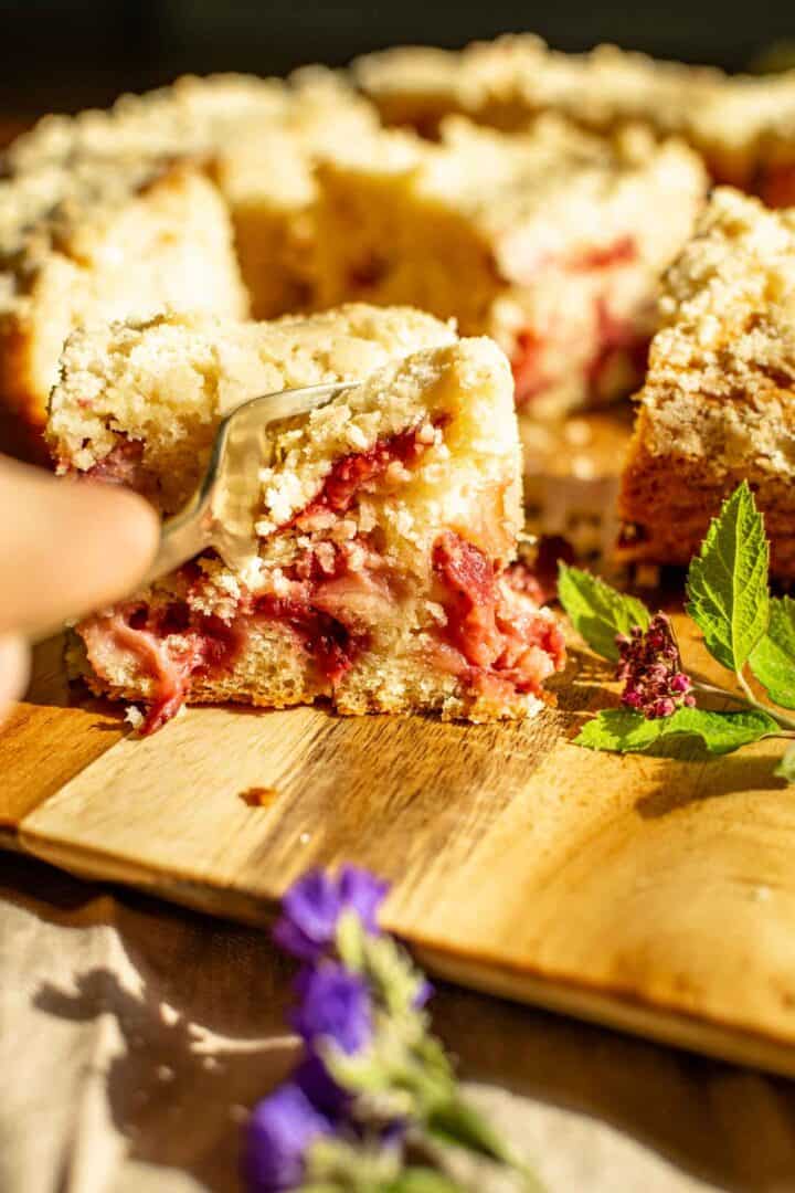 Cutting into a slice of strawberry crumb cake with a gold fork.
