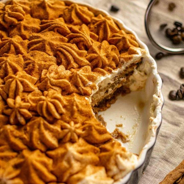 A circular dish of dirty chai tiramisu with a big scoop taken out of it; the mascarpone has been piped as little stars and dusted with cinnamon.