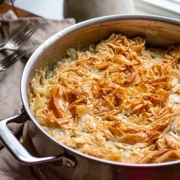 side view of phyllo pot pie in stainless steel skillet with a white vase in the background next to the window.