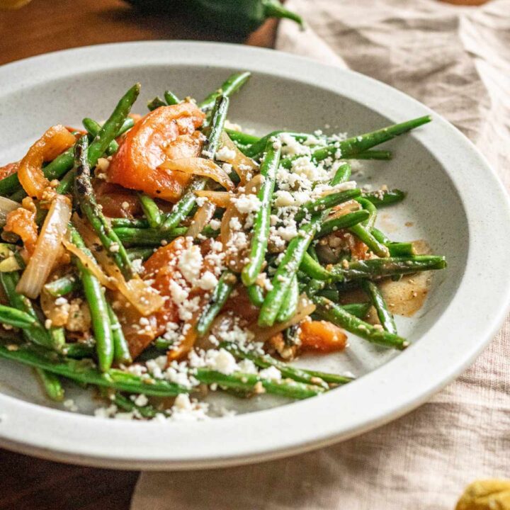 Plate of blistered green beans a la mexicana on a rimmed white plate.