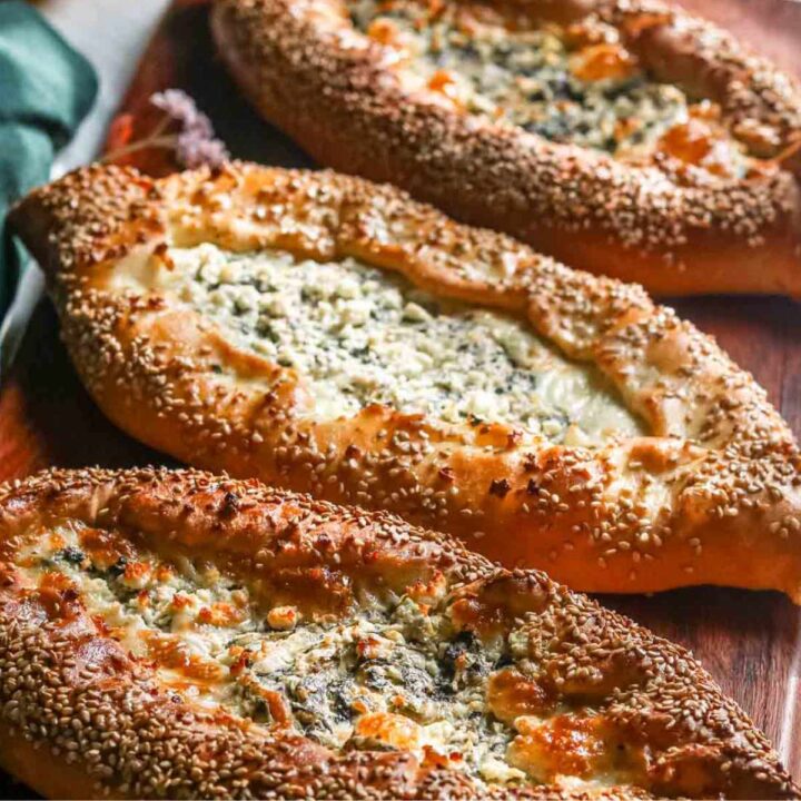 Three spinach and cheese pide on a wooden serving tray.