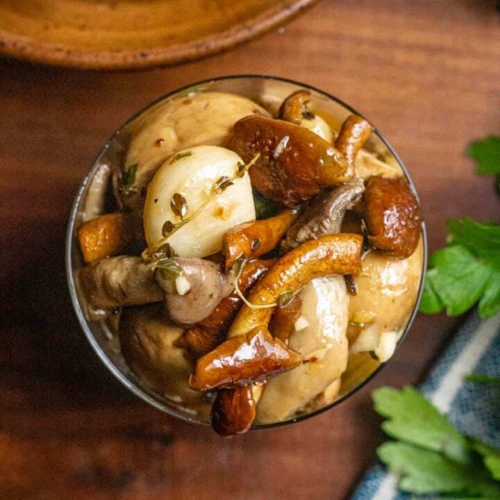 Overhead shot of marinated mushrooms in a glass dish surounded by fresh parsley and a blue striped linen kitchen towel.