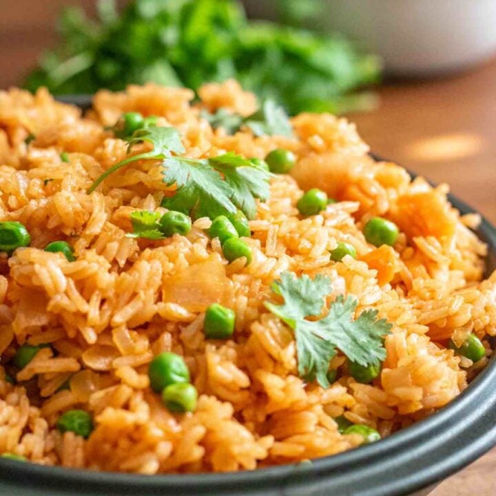 Close up of a bowl of Mexican red rice that is dotted with green peas and garnished with cilantro.