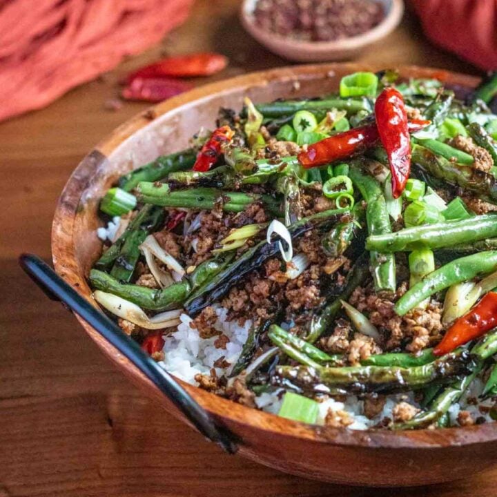 A wooden bowl of dry-fry green beans served over rice.
