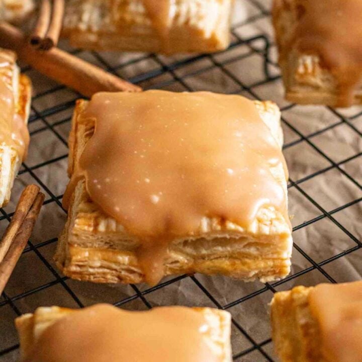 Close-up of a pumpkin pie pop tart on a cooling rack surrounded by more pop tarts and cinnamon sticks.