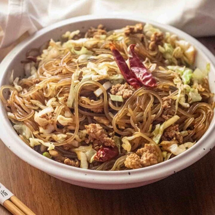 Bowl of cabbage noodle stir fry topped with 2 dried red chilies for garnish.