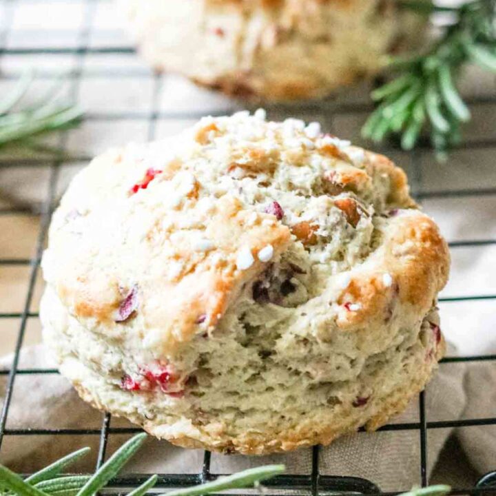 Close up of a cranberry orange scone on a black cooling rack with a sprig of rosemary in the background.