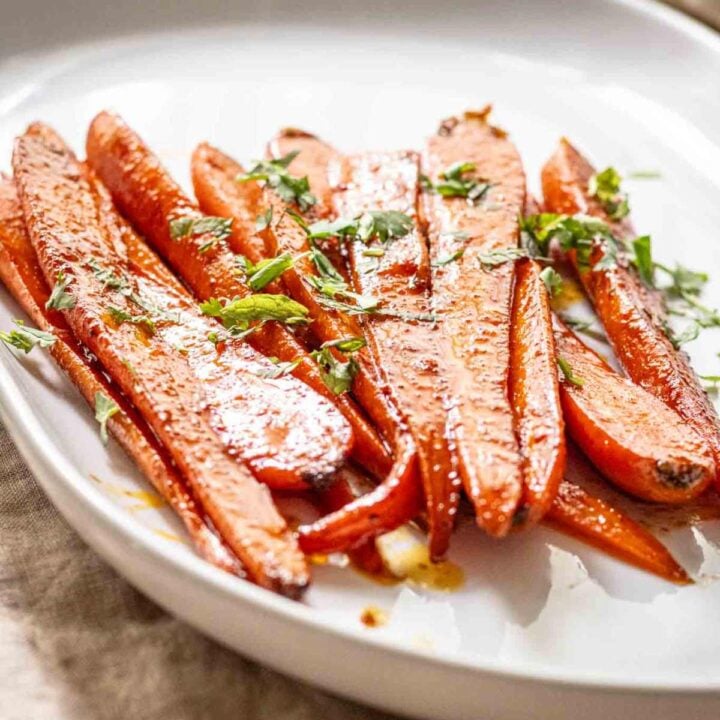 Maple glazed carrots on a white serving platter garnished with cilantro and mint.